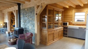 A cozy cabin interior with a stone fireplace, wooden cabinets, and a kitchen area.