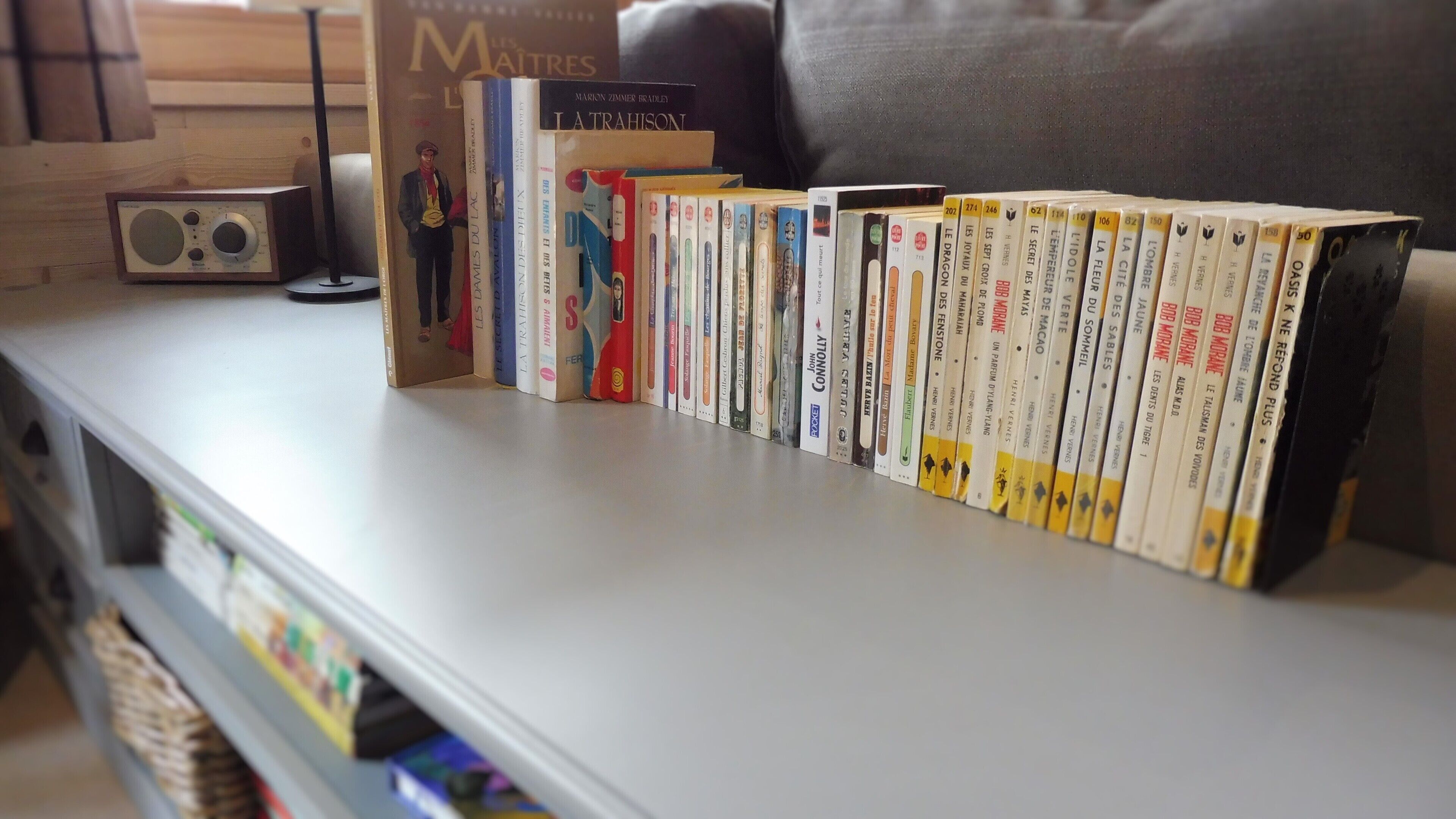 A bookshelf with a variety of books, a radio, and a pillow on a white shelf.