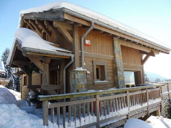 Un chalet en bois, avec des fondations en pierre, un balcon en bois et un toit recouvert de neige.