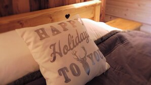 A wooden cabin interior with a bed featuring a pillow with 'HAPPY HOLIDAY TO YOU' text.