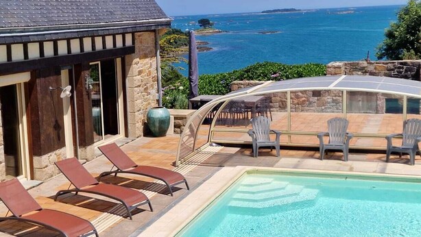 Edificio de piedra con piscina y sillas, con vistas al mar.