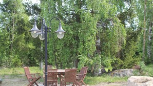 An outdoor dining area with a table and chairs, surrounded by trees and a large rock. - Jääskän Loma Kojola Apartments Alahärmä (Kauhava)