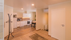 A compact kitchen with white cabinets, a microwave, and a stove. There is a dining table with chairs and a small rug on the floor. - Jääskän Loma Kojola Apartments Alahärmä (Kauhava)