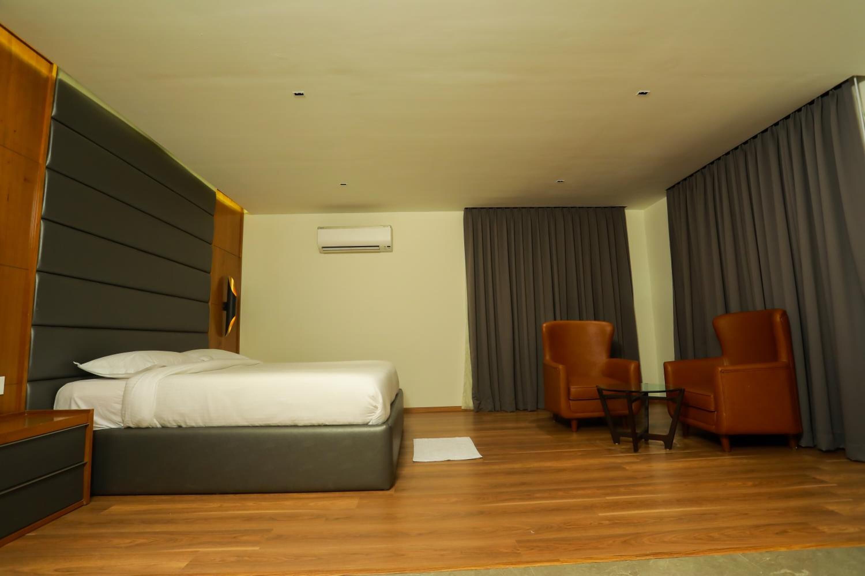 A modern hotel room with a large bed, two armchairs, a small table, and a wooden nightstand.