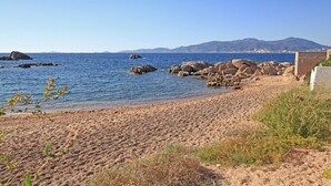 Una spiaggia sabbiosa con affioramenti rocciosi e una vista limpida sul mare e sulle montagne in lontananza.