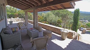 Un'area salotto esterna riparata, con mobili in vimini, un muro in pietra e vista sul paesaggio circostante.