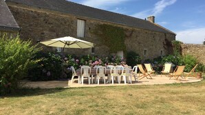 Edificio de piedra con un patio jardín que presenta una mesa, sillas, una sombrilla y plantas en macetas.
