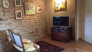 Una habitación acogedora con pared de piedra, una silla de madera, un televisor de pantalla plana sobre un mueble de madera y una alfombra en el suelo.