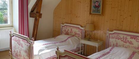 Ein Schlafzimmer mit zwei Betten, Holzwänden, einem Fenster mit roten Vorhängen und einem kleinen Nachttisch mit einer Lampe.