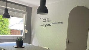 Ein Essbereich mit Tisch für zwei Personen, einem Blumentopf und einer Wand mit einem motivierenden Zitat.