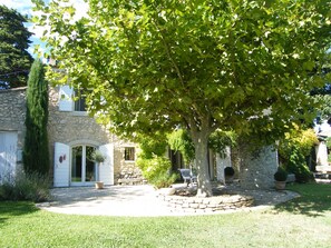 Ein Steinhaus mit kreisförmigem Zugangsweg, einem Baum in der Mitte und einem kleinen Garten.