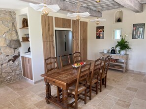 Ein Essbereich mit Holztisch und -stühlen, einer Steinsäule und einer Küche mit Holzausstattung und einem Kühlschrank.