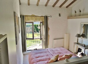 Ein Schlafzimmer mit großem Fenster, Heizkörper, Spiegel und Nachttisch mit Lampe.