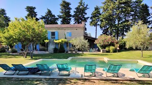 A pool with lounge chairs, a stone wall, and a house with blue shutters.