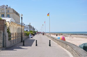 Une promenade en bord de mer, avec un sentier pavé de pierres, des bâtiments d’un côté et une plage de l’autre.