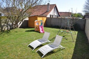 Relax in the backyard with two lounge chairs on the lush lawn, adjacent to a charming playhouse with a slide.