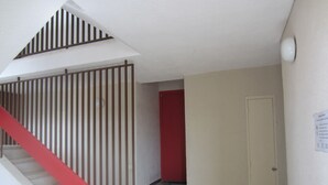 Un escalier avec une rampe rouge menant à un palier, un mur rouge et une porte fermée avec une pancarte sur le mur.