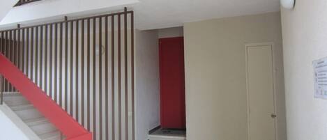 Una escalera con barandilla roja que lleva a un rellano, una pared roja y una puerta cerrada con un letrero en la pared.