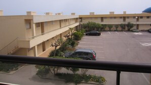 Un parking à plusieurs étages, où sont garées plusieurs voitures, entouré de verdure et bordé d’un immeuble doté d’un toit plat.