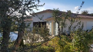 Ein Haus mit Ziegeldach, umgeben von Olivenbäumen und Sträuchern.