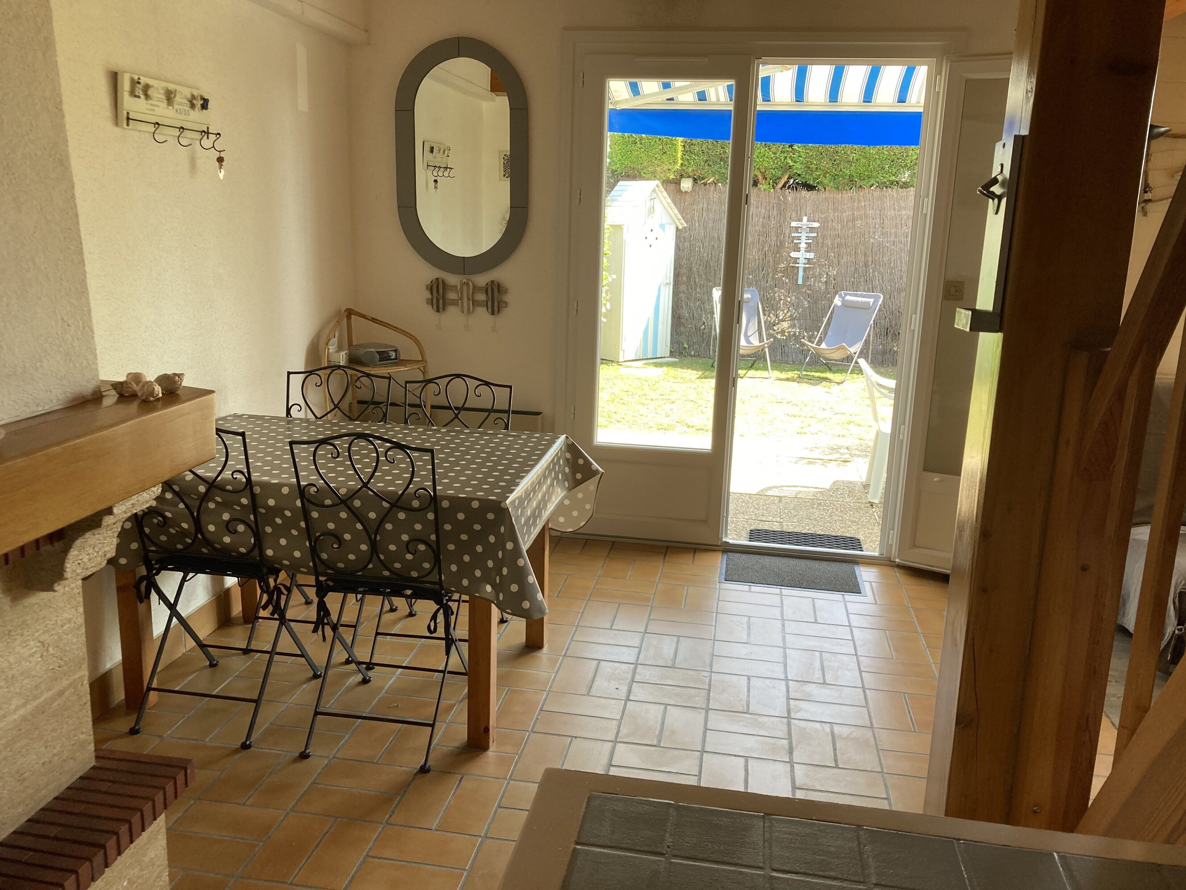 Un coin repas avec une table et des chaises, un miroir au mur et une vue sur le jardin à travers une porte coulissante.