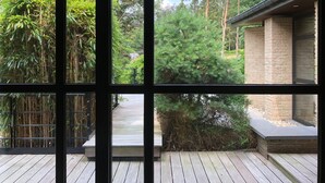 A view through a window with a wooden deck, bamboo, and a stone building.