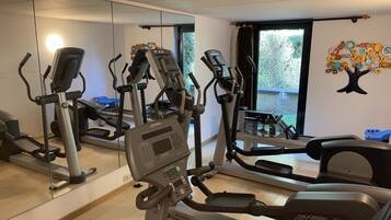 Une salle de sport équipée de plusieurs tapis de course, d’un murmiroir et d’une grande fenêtre donnant sur un espace verdoyant.