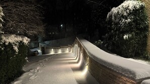 A snow-covered pathway leading to a building with a brick wall and a wooden deck.