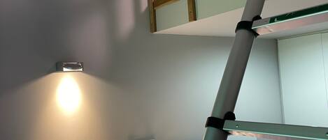 A bunk bed with a ladder, a bedside table, and a wall-mounted light fixture.