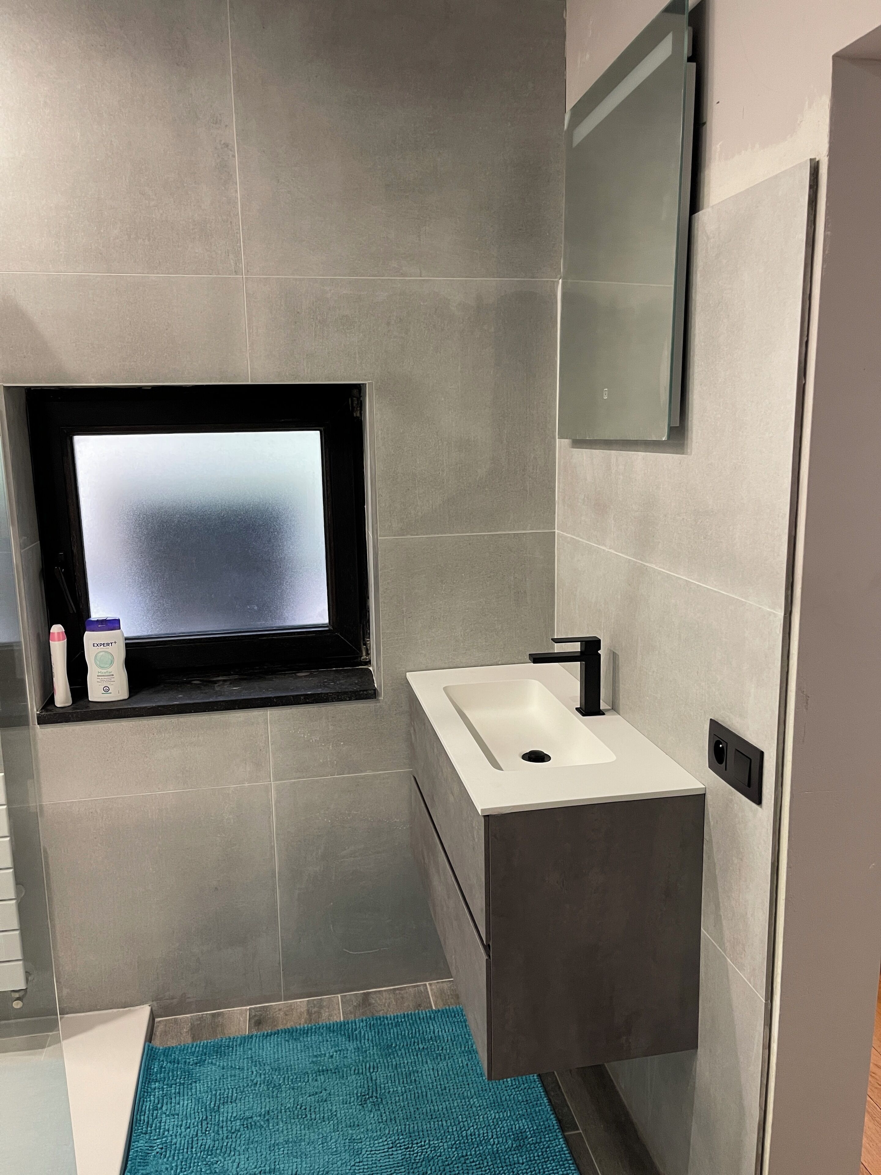 Une salle de bain moderne avec un lavabo intégré, un miroir au-dessus et une fenêtre en verre dépoli.