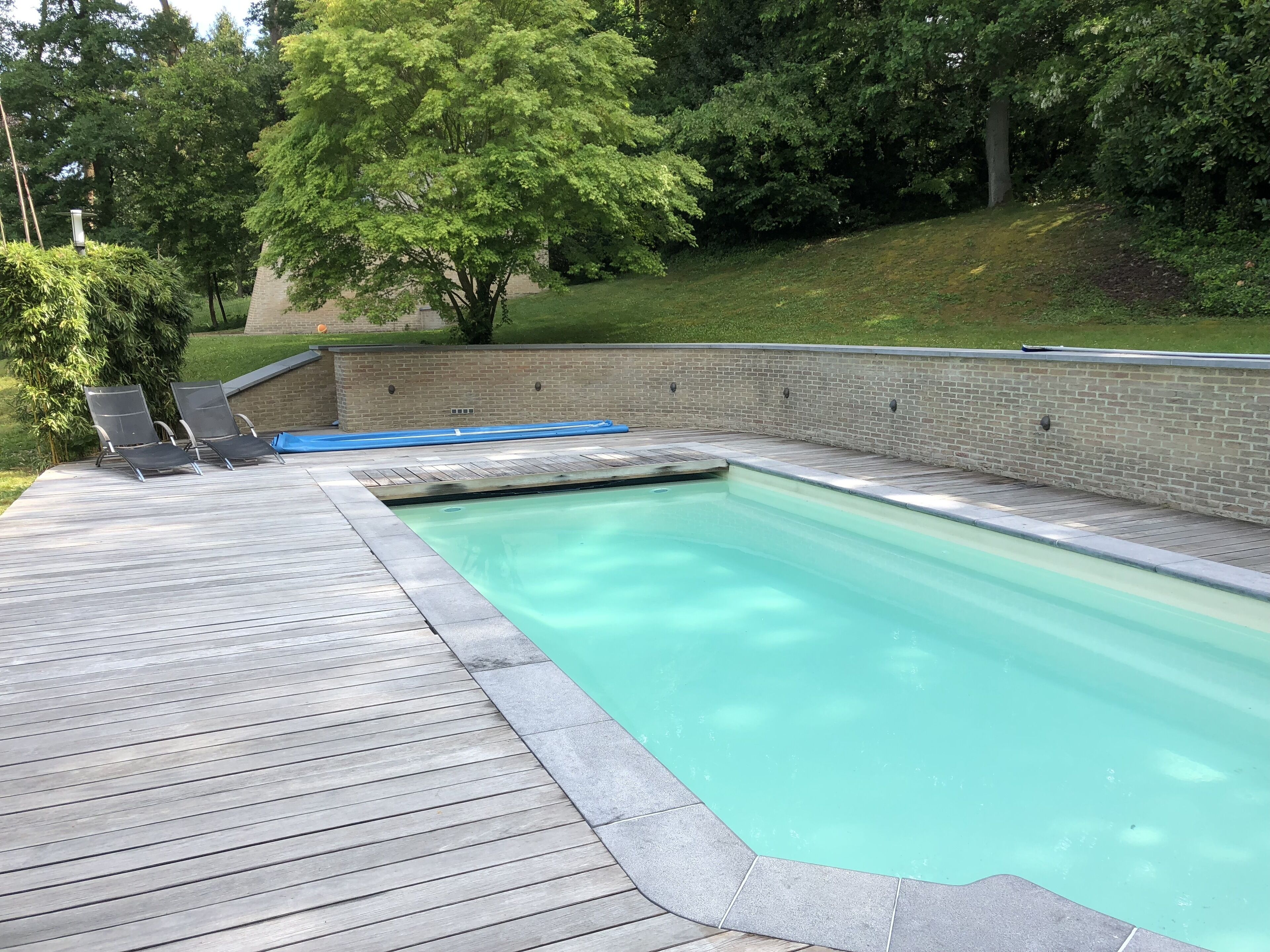 Una piscina con bordo in legno e due lettini.