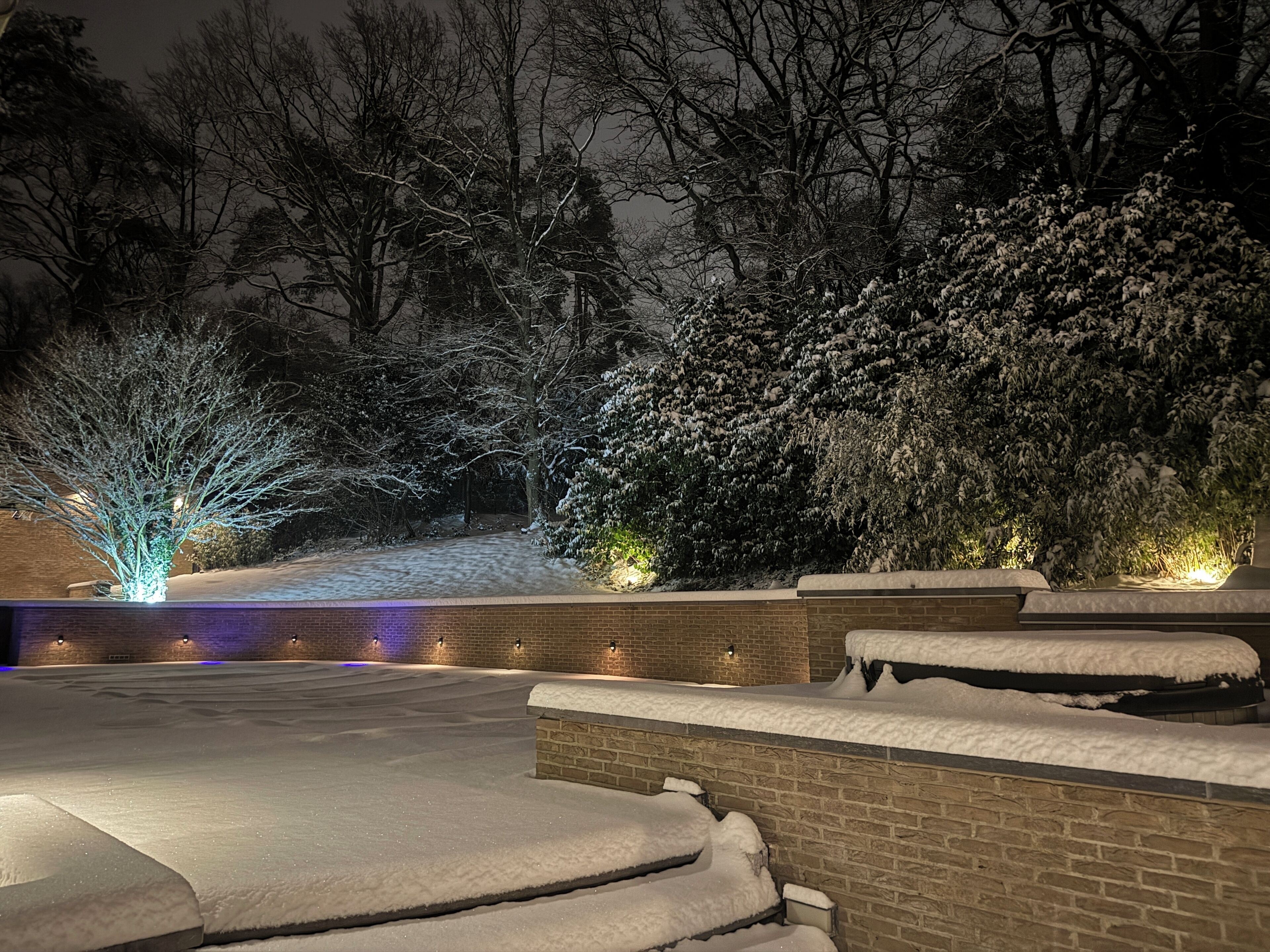 A snow-covered outdoor area with steps and brick walls, illuminated by ambient lighting.