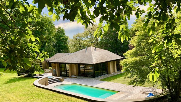 A modern house with a swimming pool, surrounded by lush greenery and a covered patio.