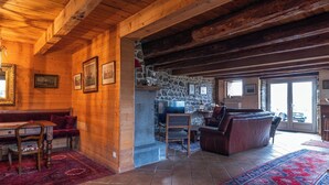 A cozy log cabin interior with a stone fireplace, wooden beams, and a red and blue patterned rug. - 🌟Parenthèse nature en Auvergne: Maison typique au panorama exceptionnel-10 pers (saint- sauves d'Auvergne)