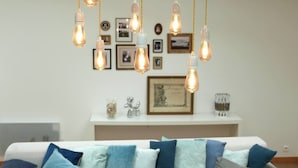 A room with a white sofa adorned with blue and grey cushions, a white console table with framed pictures and decorative items, and multiple hanging Edison-style light bulbs. - Village house Scandinavian charm (Carantec)