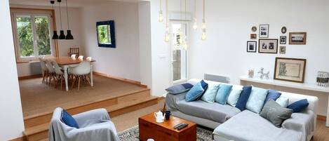 A modern living room with a grey sofa, two armchairs, a coffee table, and a dining area with a table and chairs.