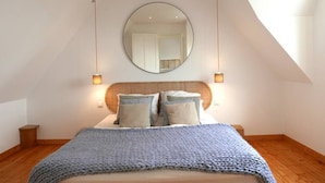 A bedroom with a large bed, a round mirror above the bed, and two wall-mounted lamps. - Village house Scandinavian charm (Carantec)