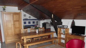 Une cuisine chaleureuse avec des meubles de rangement en bois, une table à manger avec des bancs, une chaise rouge et un téléviseur posé sur un meuble en bois.