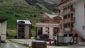 Un immeuble avec une enseigne indiquant « Résidence l’Aperon » et un espace de stationnement où sont garées des voitures.