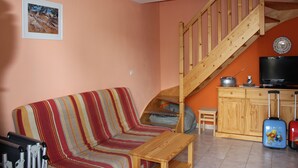 Una sala de estar con un sofá a rayas, una mesa de madera, una escalera, un televisor y un mueble.