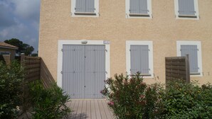 Un edificio de dos plantas con fachada color crema, varias ventanas con contraventanas y una puerta central grande.