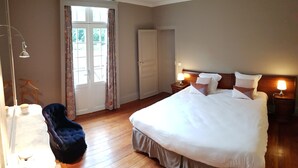 A bedroom with a large bed, two bedside lamps, a chair, a wardrobe, and a door with curtains. - Manoir du Chambellan (Les Baux-Sainte-Croix)