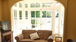 A living room with a sofa, a coffee table, a television, and a window with a view of greenery. - Manoir du Chambellan (Les Baux-Sainte-Croix)