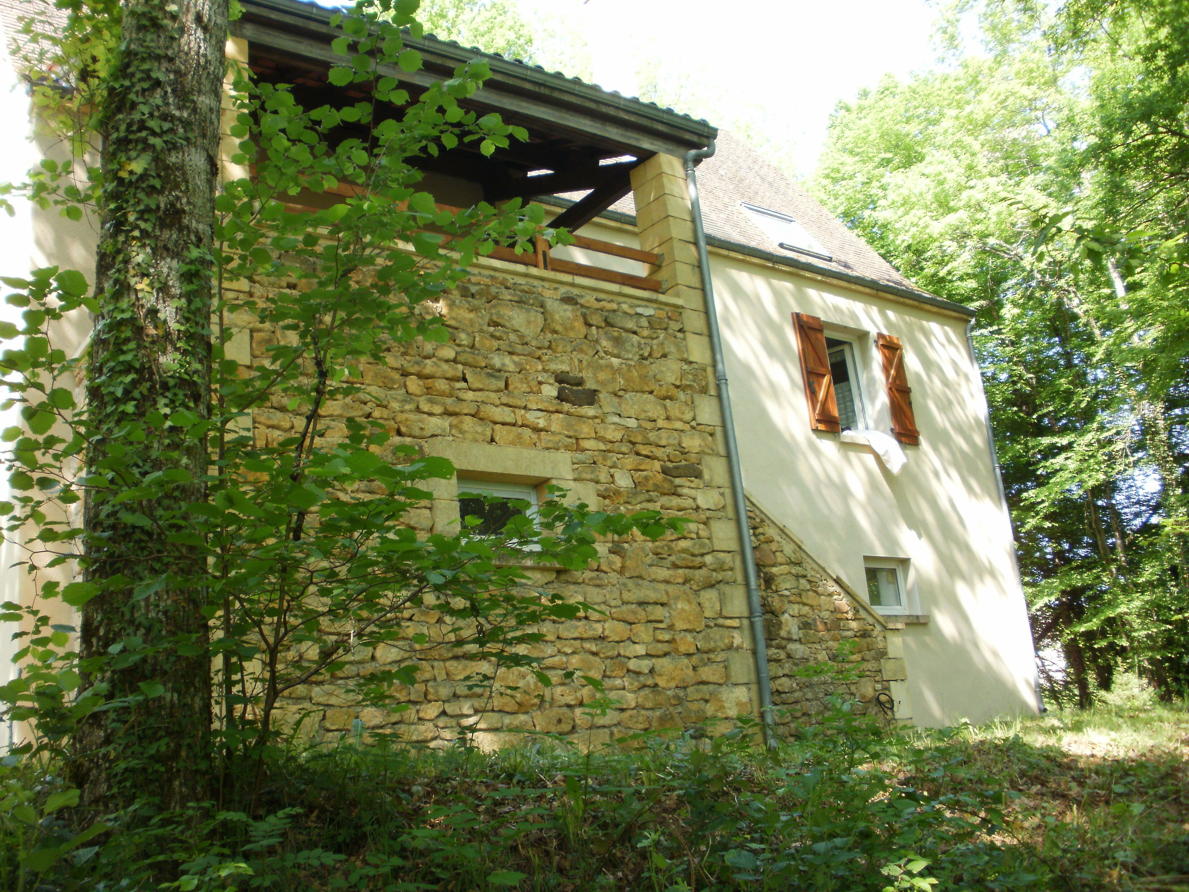 A stone building with a sloped roof, wooden beams, and a window with shutters.