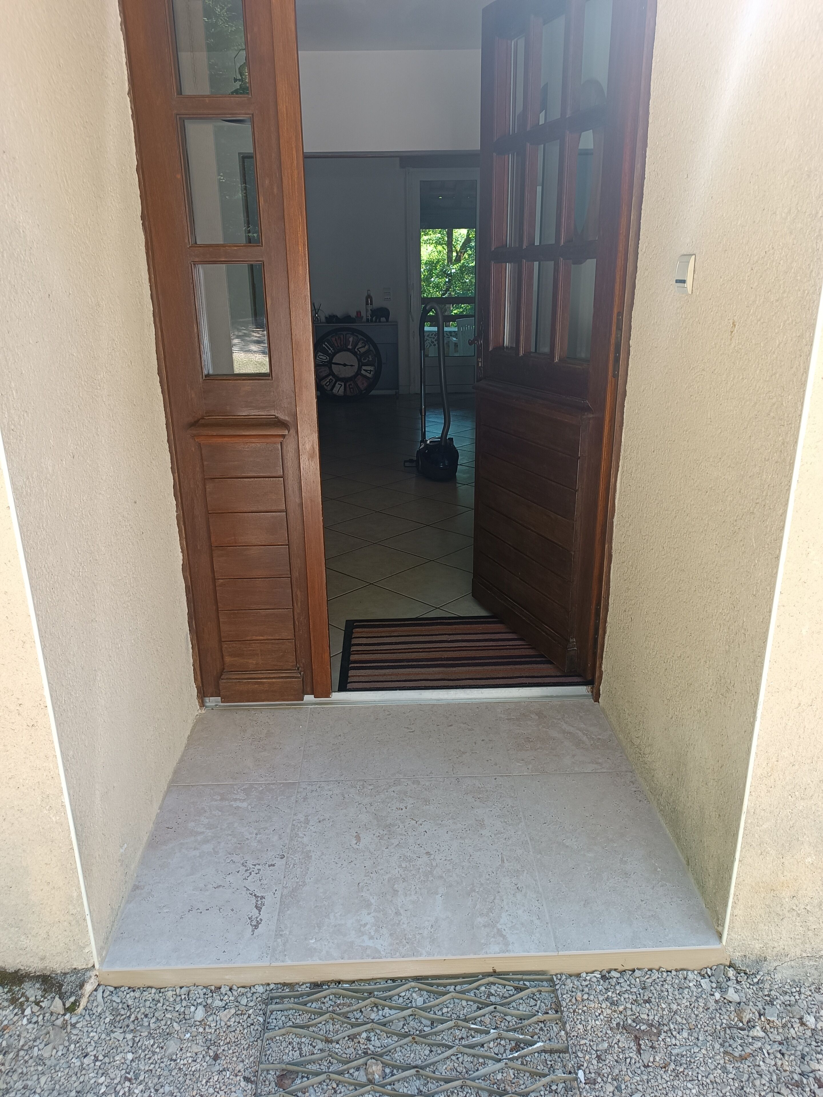 Un pasillo con puerta de madera, piso de baldosas y una alfombra pequeña.