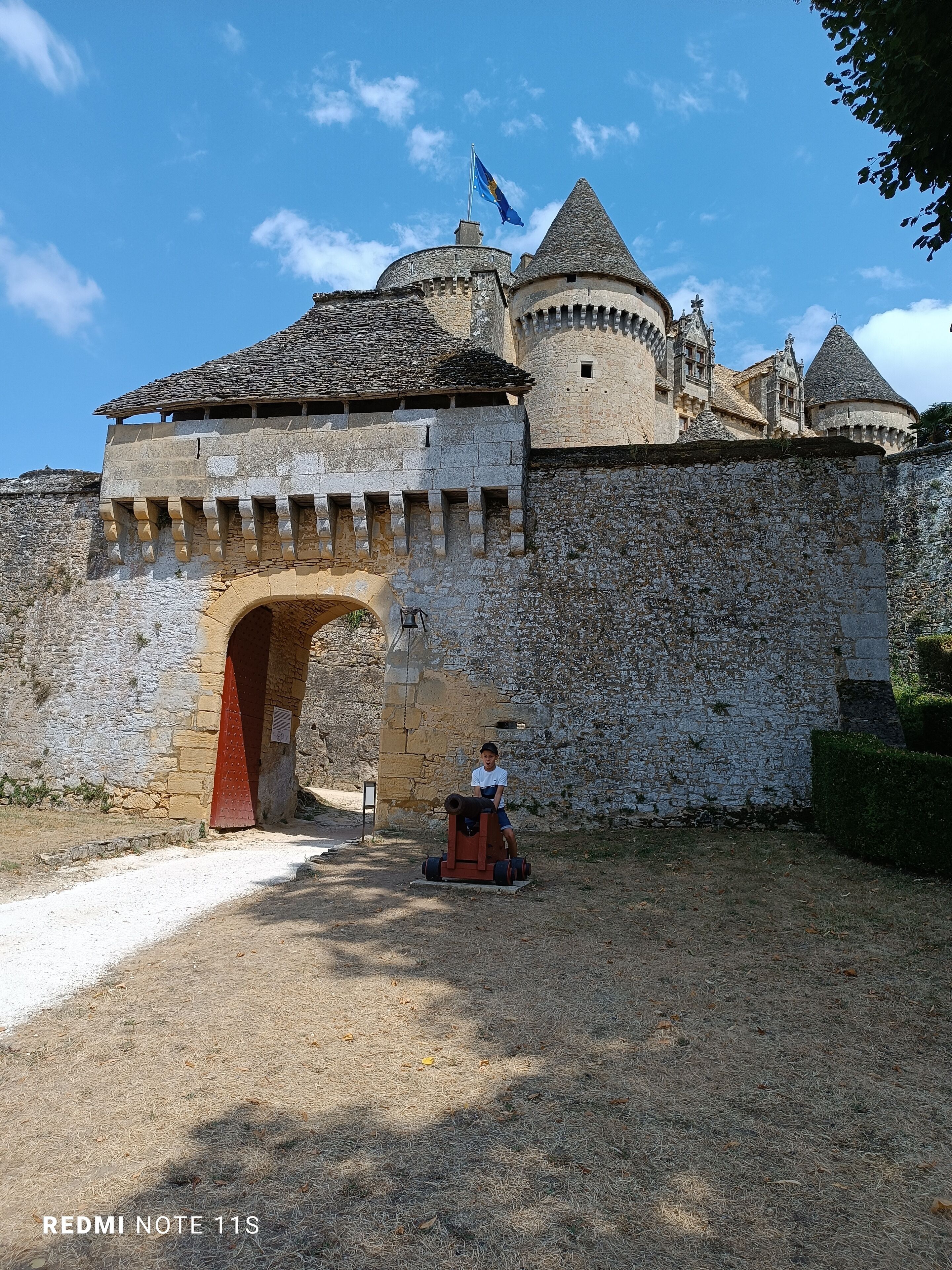 A historic stone castle with a large archway entrance, a flag, and a cannon.
