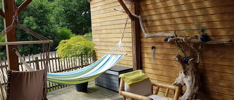 Une terrasse en bois avec un hamac, une chaise et une table.