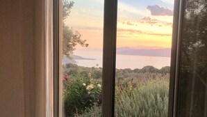 A room with a bed and a large sliding glass door leading to a balcony with a view of the sea and hills. - 2 villas together for an exceptional view with private pool (SKIATHOS)