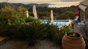 A pool with a view of the sea and hills, surrounded by plants and umbrellas. - 2 villas together for an exceptional view with private pool (SKIATHOS)