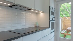 Cocina moderna con armarios blancos, encimera negra y vista a una terraza de madera a través de una puerta de vidrio.